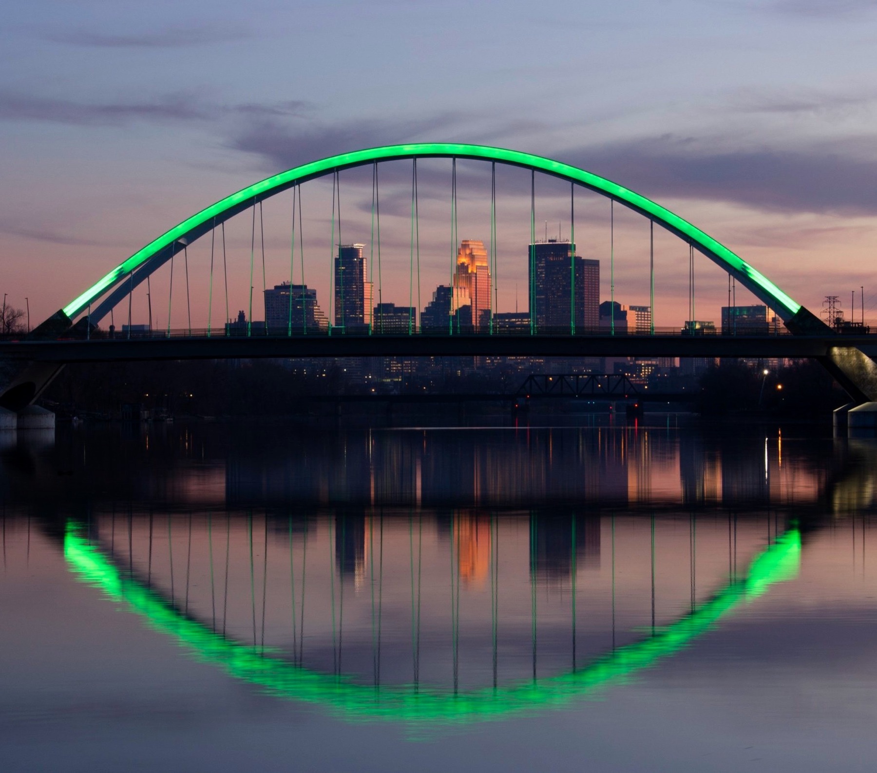 The Lowry Avenue Bridge arch and its reflection lit green over the Mississippi River in Hennepin County, Minn.