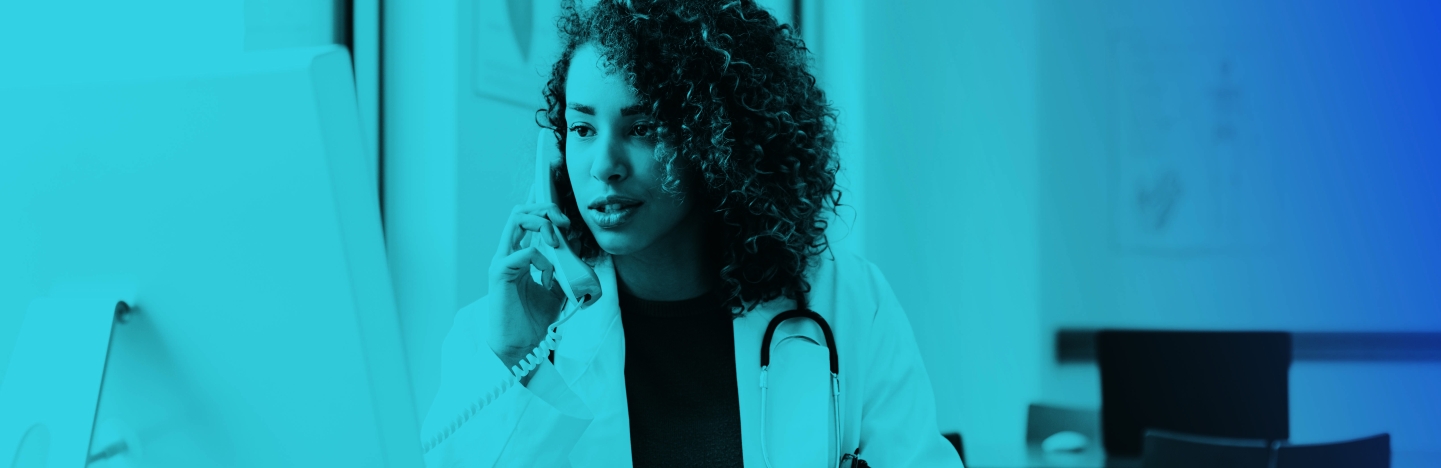 Physician at desk looking at computer talking on phone