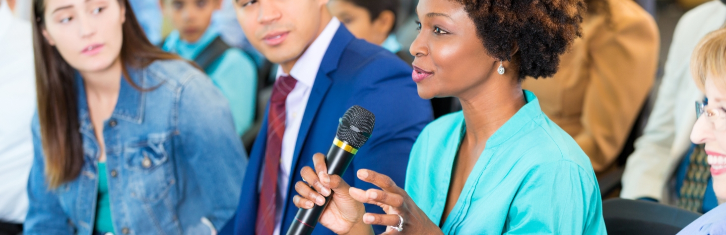A woman speaks into a microphone while others listen in