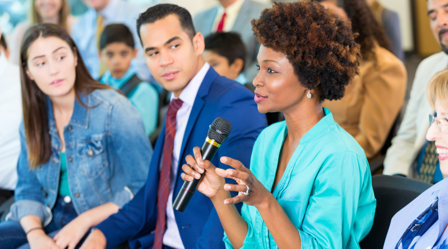 A woman speaks into a microphone while others listen in