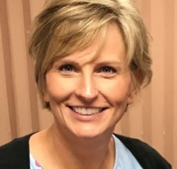 Individual with blonde hair smiling against tan backdrop