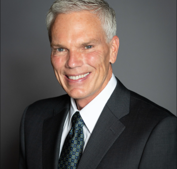 Individual with light hair smiling wearing suit and tie