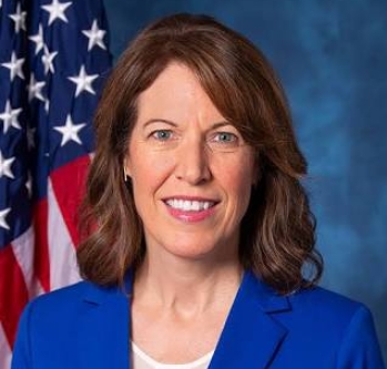 Federal official with brown hair smiling in front of the U.S. flag