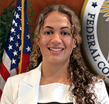 individual smiling in front of American Flag and FCC seal