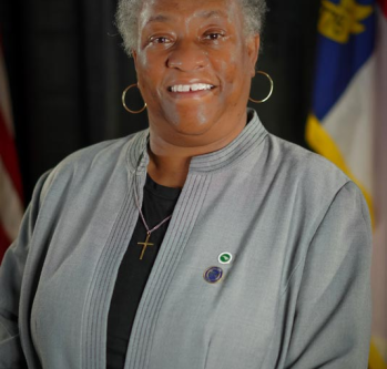 individual smiling in gray jacket in front of NC flag