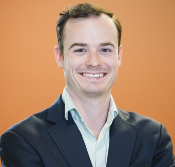 Picture of Seamus Dowdall smiling in a suit jacket and button down with orange background
