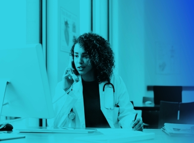 Physician at desk looking at computer talking on phone