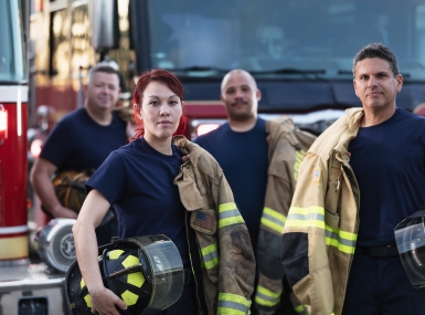 Female firefighter and group of firemen with fire trucks