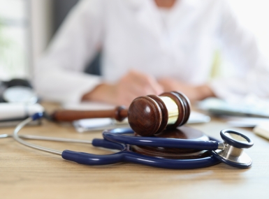 Closeup of judge gavel of stethoscope doctor in background writing notes