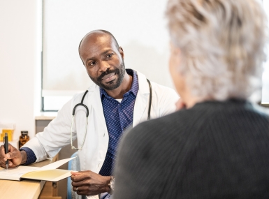 Black mid adult male doctor with notepad and pen talking to a patient