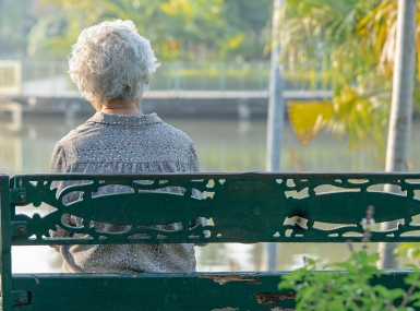 Elderly woman sitting alone on bench in autumn park