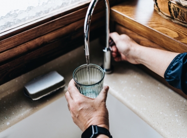Personal perspective of man filling a glass of filtered water right from the tap in the kitchen at home