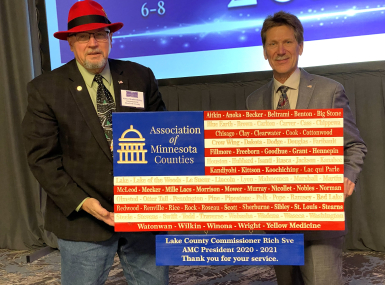 Blue Earth County Commissioner Vance Stuehrenberg presents Lake County Commissioner Rich Sve with a flag in honor of Sve's term as Association of Minnesota Counties president. 