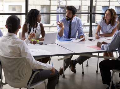 Office workers sit around a table for a meeting