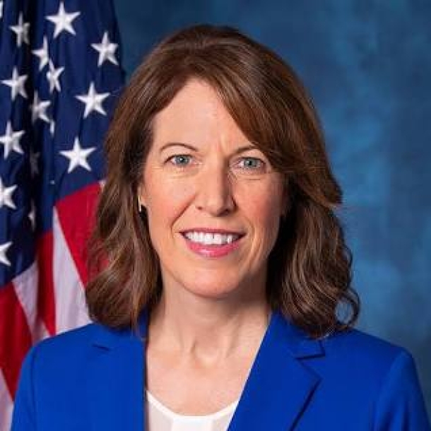 Federal official with brown hair smiling in front of the U.S. flag