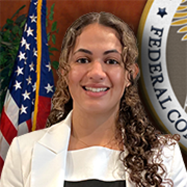 individual smiling in front of American Flag and FCC seal