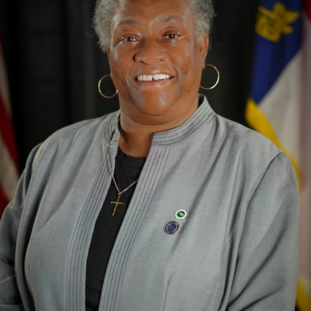 individual smiling in gray jacket in front of NC flag