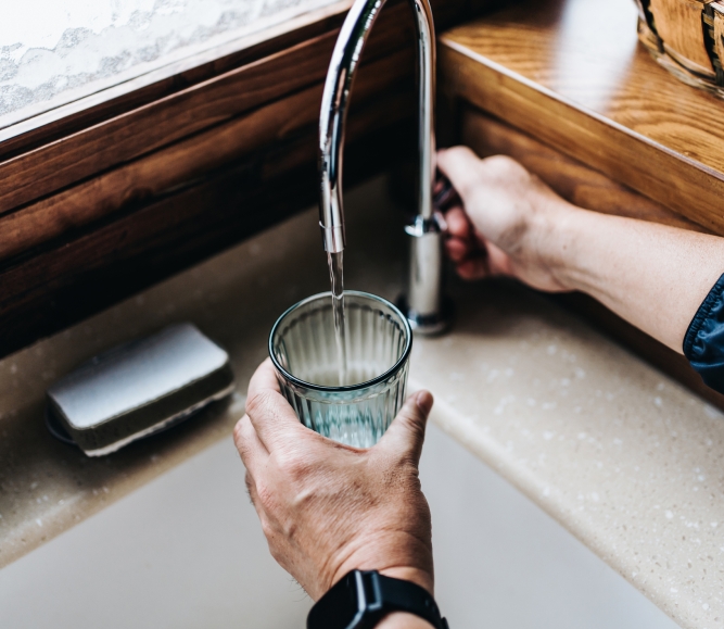 Personal perspective of man filling a glass of filtered water right from the tap in the kitchen at home