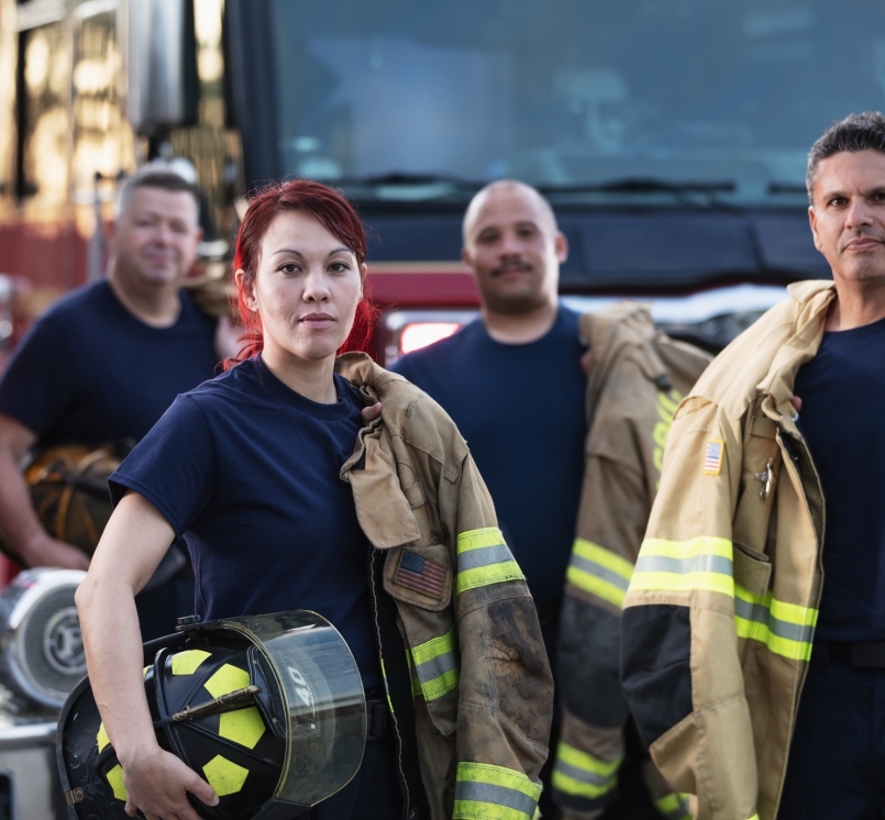 Female firefighter and group of firemen with fire trucks