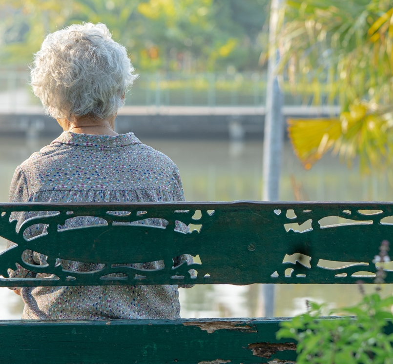 Elderly woman sitting alone on bench in autumn park
