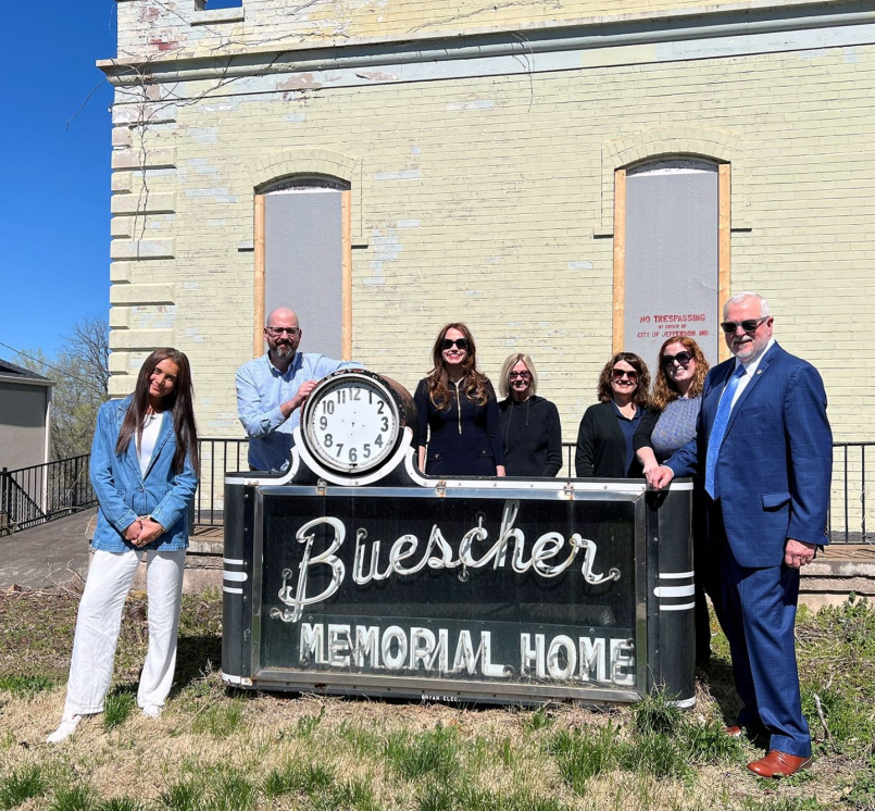 Staff of the Missouri Association of Counties stand in front of the historic “Buescher Memorial Home” sign located at 429 Capitol Ave. in Jefferson City. From left: Intern Isabella Grander, Deputy Director David Owen, Member Engagement Director Carah Bright, Finance and Operations Manager Cindy Wells, Administrative Support Assistant Charlotte Onstott, Event and Marketing Coordinator Meredith Melahn and Executive Director Steve Hobbs. Not pictured due to traveling: Trust Risk Manager Sean McGonigle
