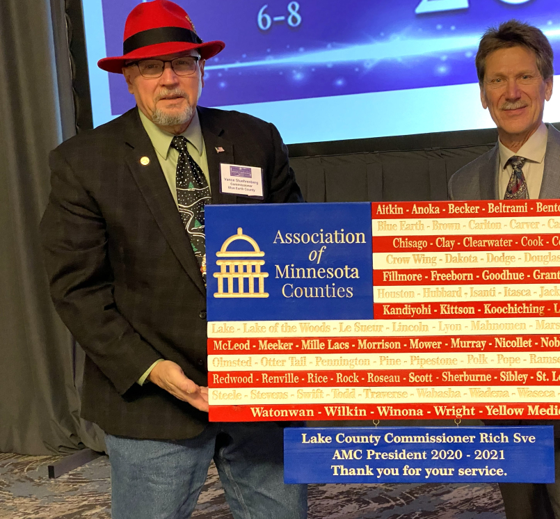 Blue Earth County Commissioner Vance Stuehrenberg presents Lake County Commissioner Rich Sve with a flag in honor of Sve's term as Association of Minnesota Counties president. 
