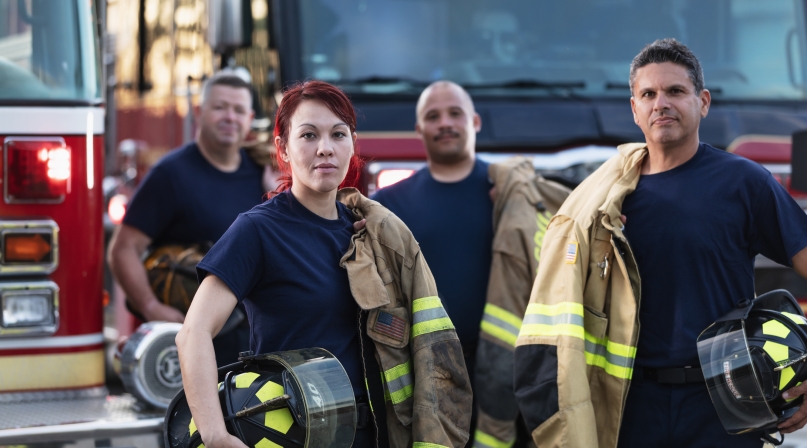 Female firefighter and group of firemen with fire trucks