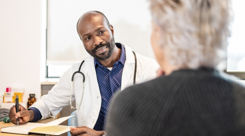 Black mid adult male doctor with notepad and pen talking to a patient