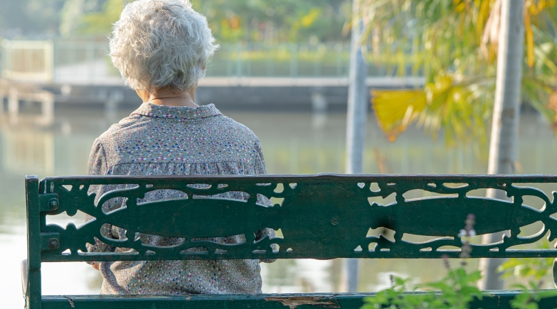 Elderly woman sitting alone on bench in autumn park