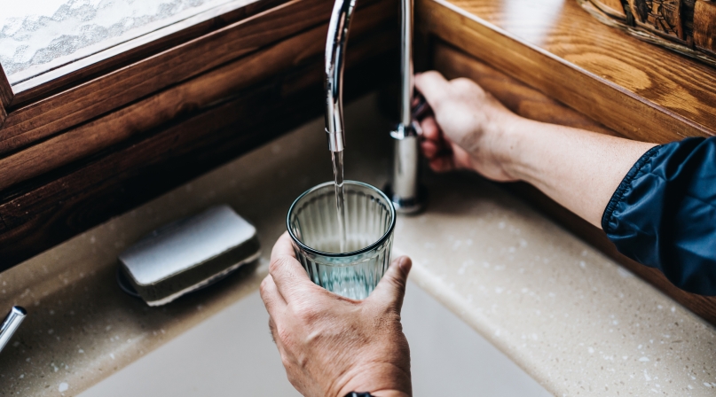 Personal perspective of man filling a glass of filtered water right from the tap in the kitchen at home